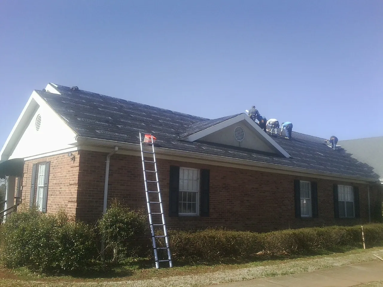 Crew tearing shingles off a brick ranch roof with a ladder set — Emergency Roof Repair work by our crew in Kutztown