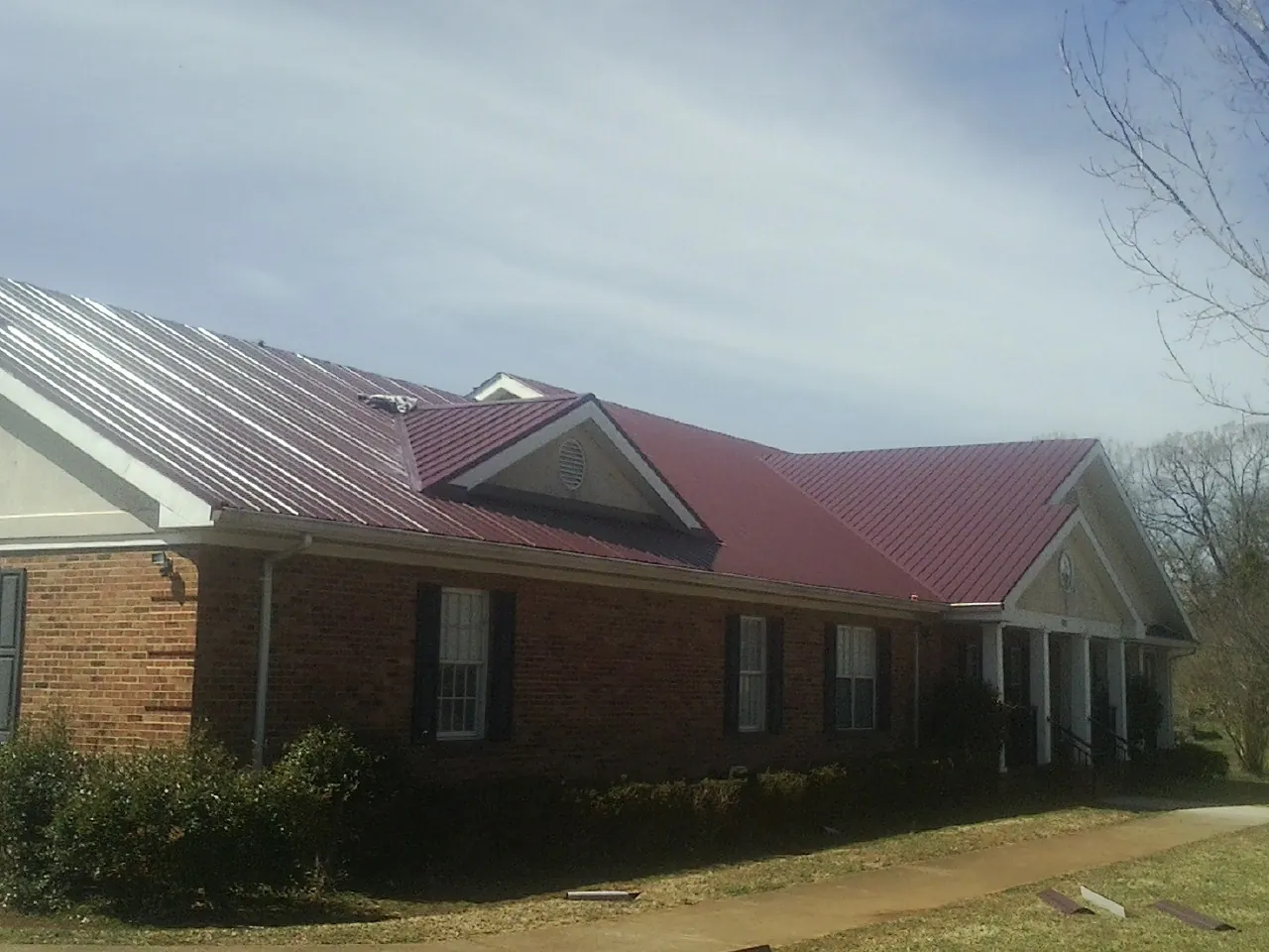 Red metal roof with gabled entries on a long brick building, from a Hail Damage Roof Repair job in Kutztown