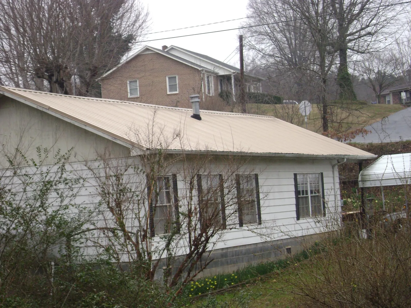 Tan metal roof on a white sided house set into a hillside — Commercial Roofing by Roofing Brothers in Kutztown